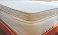 A close-up of a cream-colored quilted mattress topper resting on a Archetype mattress on a wooden bed frame.