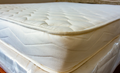 A close-up shot of a Cazenovia Mattress quilted mattress topper or mattress corner, showing the tufted top surface and stitched side edge.