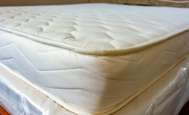 A close-up shot of a Cazenovia Mattress quilted mattress topper or mattress corner, showing the tufted top surface and stitched side edge.