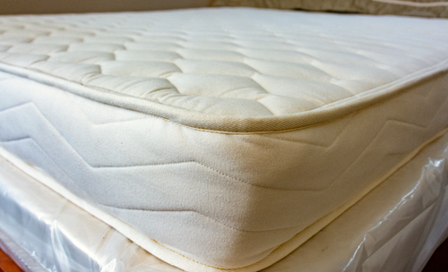 A close-up shot of a Cazenovia Mattress quilted mattress topper or mattress corner, showing the tufted top surface and stitched side edge.
