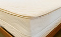 A close-up of a quilted mattress topper or mattress corner, showing the cream-colored fabric texture and the wooden bed frame.